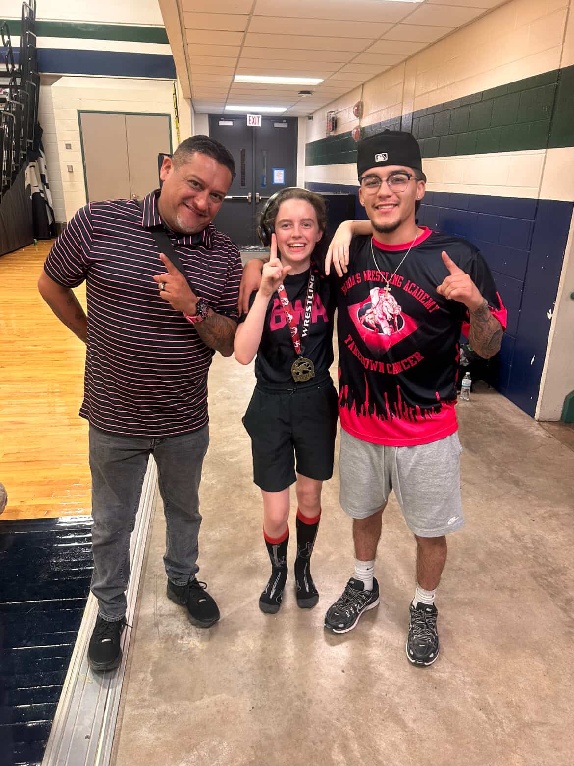 Young wrestler celebrating a win with her medal alongside her coaches